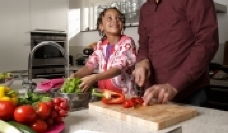 vader en dochter die in de keuken de maaltijd voorbereiden (groente en kip snijden)