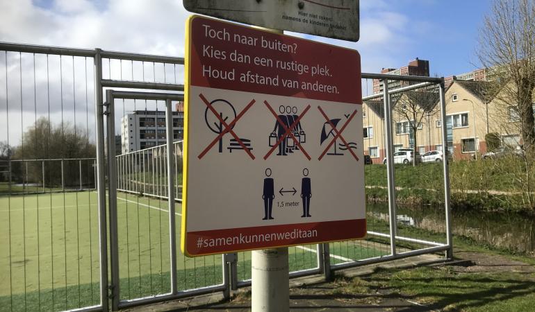 Tijdelijk bord van de gemeente Den Haag, bevestigd aan een paal bij een sportveld, dat wijst op de maatregelen die zijn genomen in het kader van de aanpak van het coronavirus.