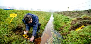 Veldonderzoeker vangt water op uit drain bij sloot