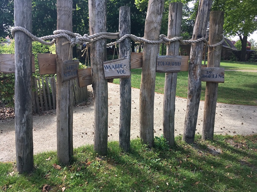 Een hek van palen en touw met daarop houten bordjes 