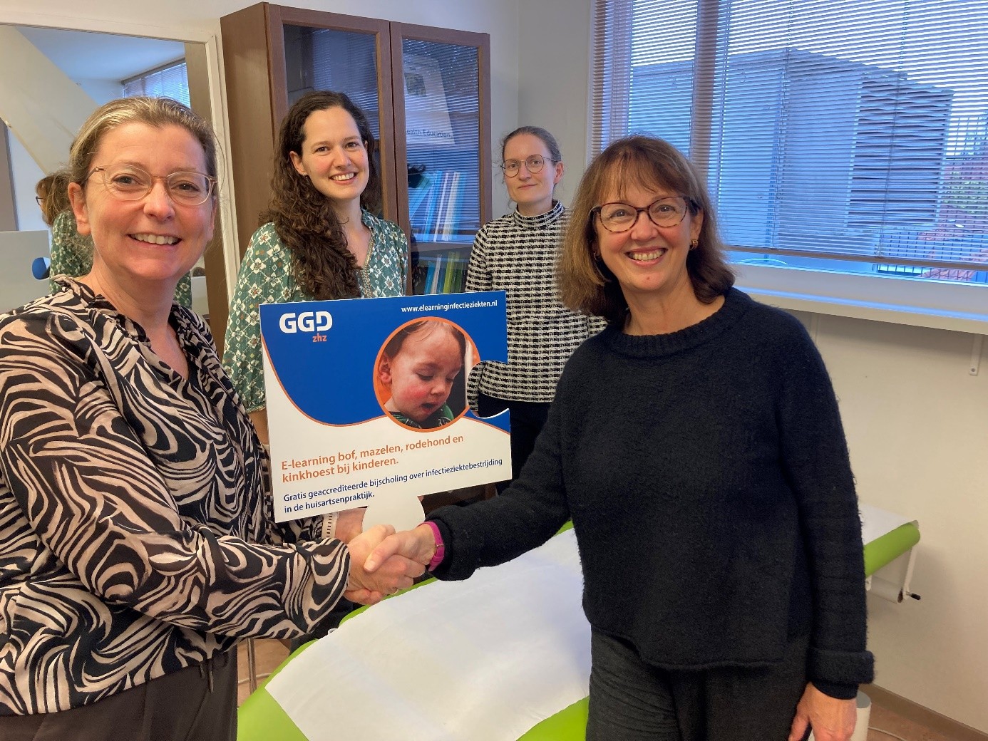 Ellen Verspui Chief Medical Officer DG&J ZHZ/GGD ZHZ en RAC Zuid-Holland (links) overhandigt de e-learning aan huisarts Florence Guibert Buiron uit Dordrecht (rechts). Op de achtergrond Joan Roozemond en Myriam den Oudsten, zij werkten als verpleegkundige M+G/IZB en als arts IZB mee aan de ontwikkeling van de e-learning.