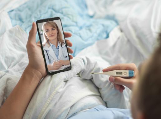 een patient ligt in het ziekenhuisbed en praat via beeldtelefoon (bijv. Skype) et de arts.