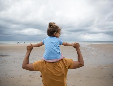Meisje op schouders van vader op strand