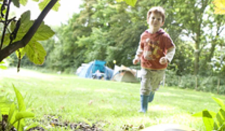 Jongen loopt op camping naar een bal die in de bosjes ligt.