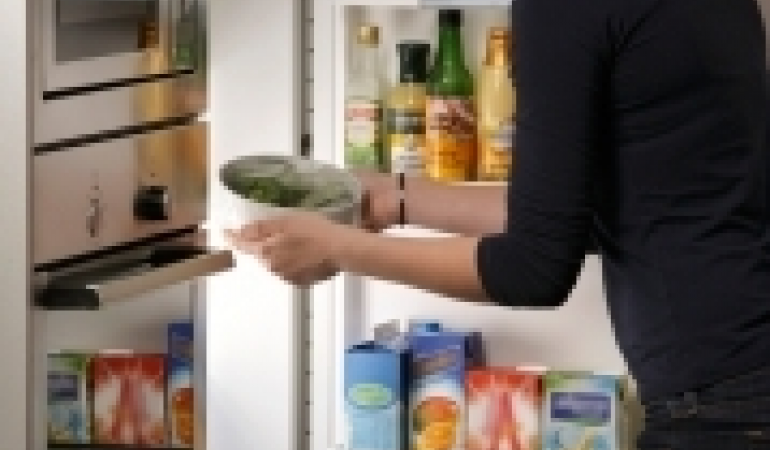 vrouw die overgebleven groenten in een afgesloten bakje terugzet in de koelkast