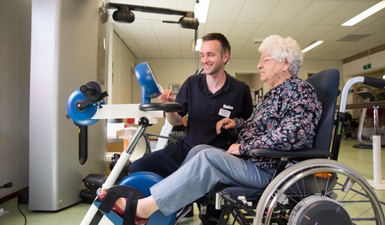 Een dame in een rolstoel samen met een fysiotherapeut