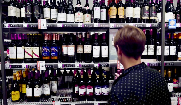 Vrouw voor schap met wijn in supermarkt