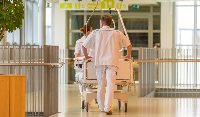 Verpleger rijdt ziekenhuisbed door gang van ziekenhuis