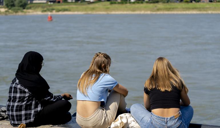 Jongeren zitten bij een rivier in de zon
