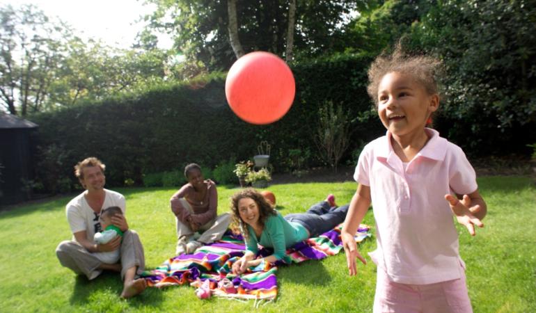 Meisje speelt met bal terwijl een gezin op de achtergrond op een picknickkleed ligt