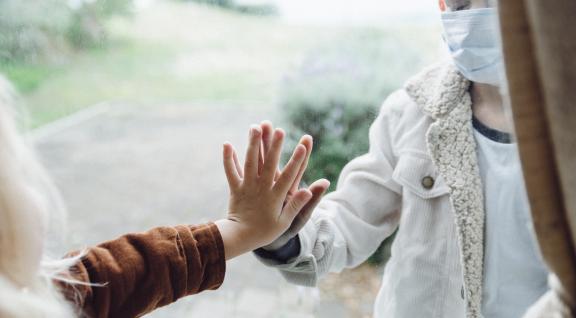 Handen tegen het raam van oudere (binnen) en kind (buiten)