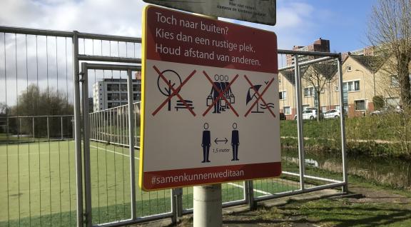 Tijdelijk bord van de gemeente Den Haag, bevestigd aan een paal bij een sportveld, dat wijst op de maatregelen die zijn genomen in het kader van de aanpak van het coronavirus.