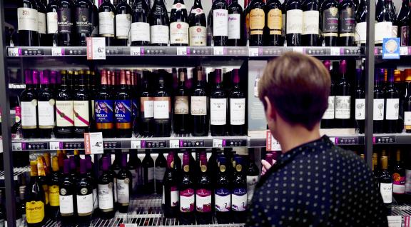 Vrouw voor schap met wijn in supermarkt