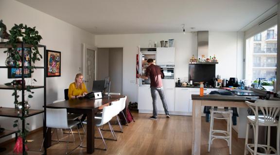 Vrouw aan het thuiswerken, man aan het koken