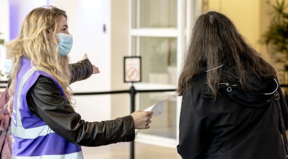 GGD medewerkster wijst vrouw de weg bij COVID-19 vaccinatie locatie