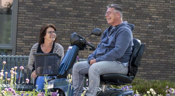 Man in scootmobiel en vrouw zitten in een tuin