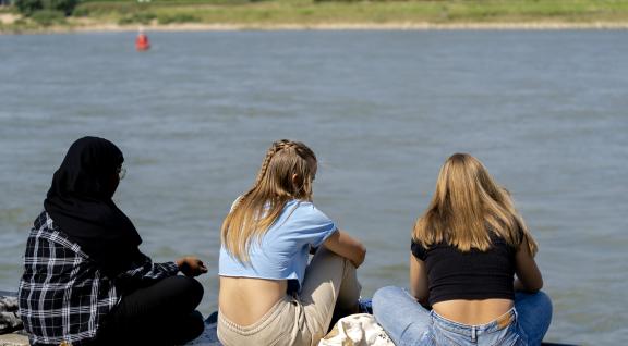 Jongeren zitten bij een rivier in de zon