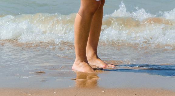 Meisje met blote voeten in de branding. Alleen de benen zijn te zien.