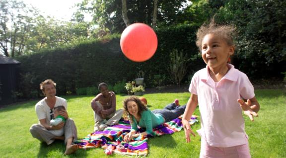 Meisje speelt met bal terwijl een gezin op de achtergrond op een picknickkleed ligt