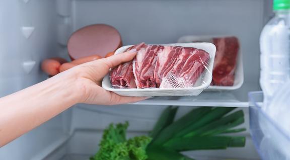 Iemand legt een bakje vlees in de koelkast