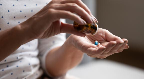 In beeld twee handen van een vrouw die 2 antibiotica pillen neemt