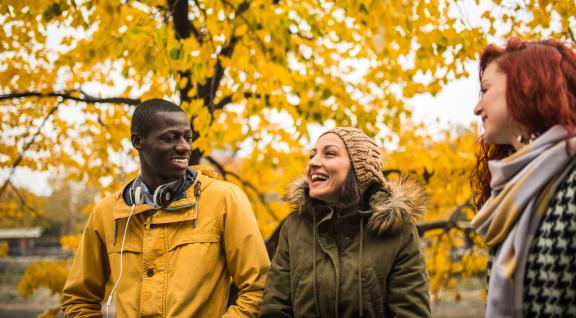 Die jongeren staan te praten met op de achtergrond een boom met gele blaadjes